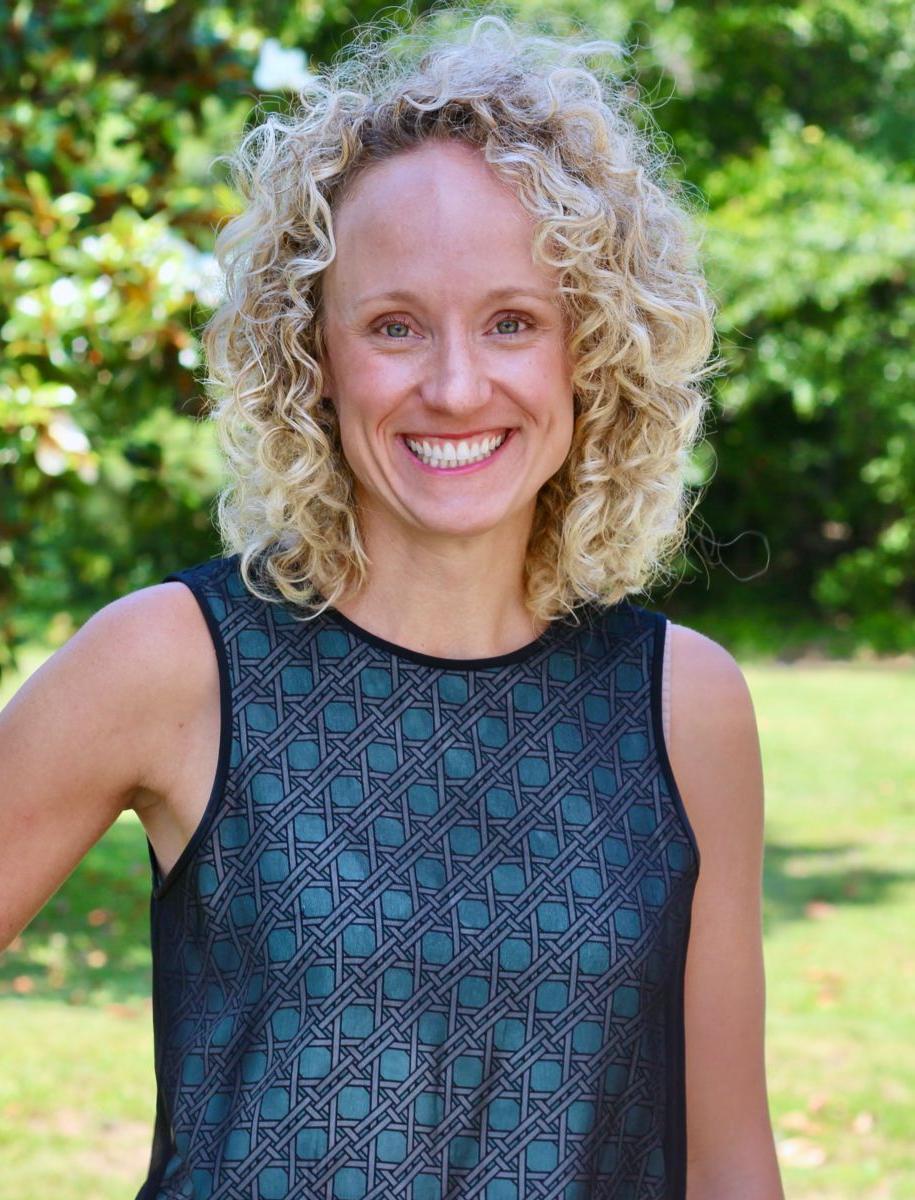 Ms. Jane Marie Kinsey, a Caucasian female with curly blonde hair smiles wearing a dark green dress with a grey lattice pattern.