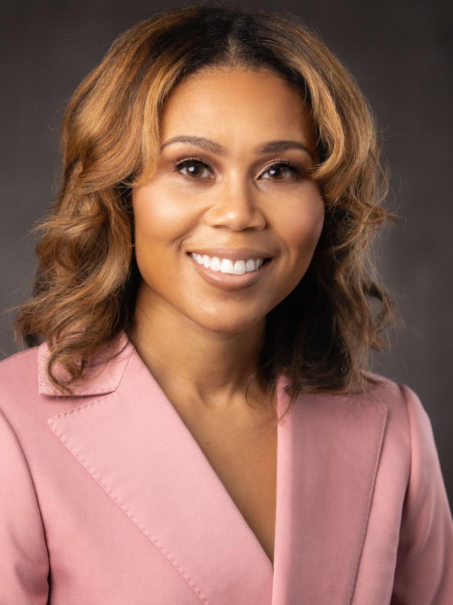 Ms. Katrell Nash, an African American female with long caramel colored hair, smiles wearing a pink suit jacket on a grey background.